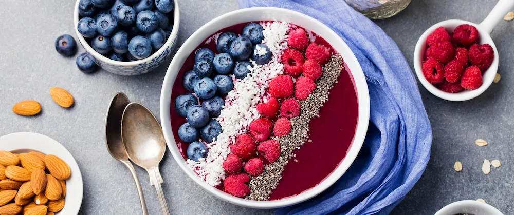 Antioxidant-rich organic avocado and mixed berry smoothie bowl, topped with chia seeds, fresh berries, and a line of shredded coconut, served alongside raw almonds.