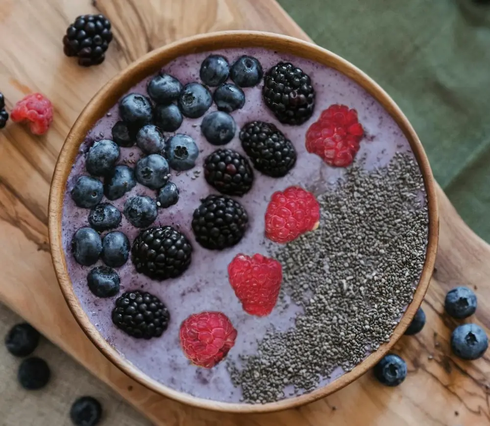 A close-up square view of the high-protein organic berry smoothie recipe bowl, highlighting distinct rows of dark blueberries, glossy blackberries, red raspberries, and fine chia seeds.