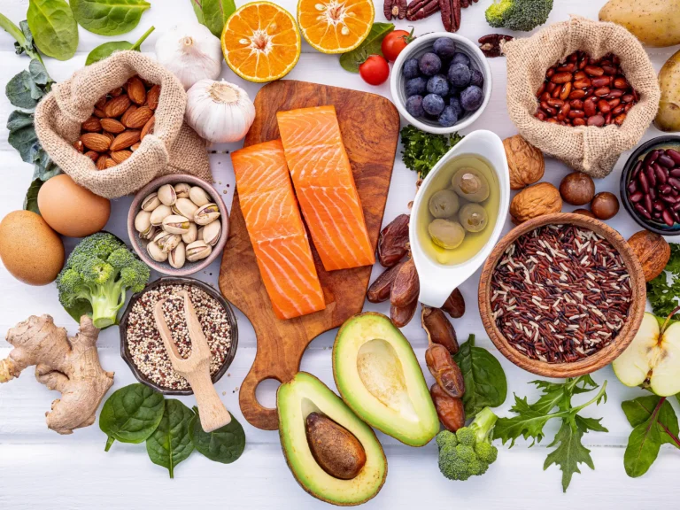 Flat lay of fatty liver healing foods including salmon, avocado, berries, nuts, citrus, garlic, olive oil, and leafy greens