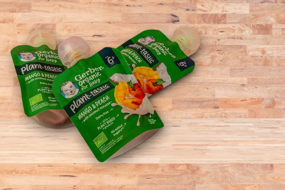 Three Gerber Organic baby food pouches on a wooden table displaying clean ingredients and the European Union organic leaf logo.
