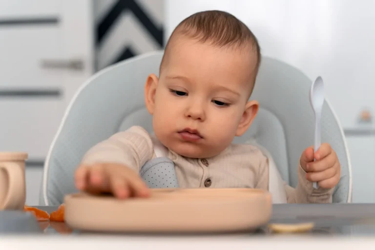 Baby sitting in high chair exploring first solid foods with spoon and plate