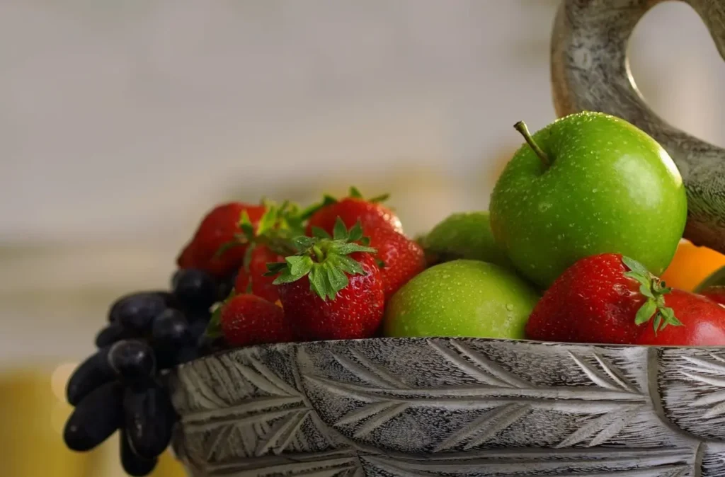 Fresh strawberries, apples, and grapes in a decorative bowl — examples of EWG Dirty Dozen foods with high pesticide levels.