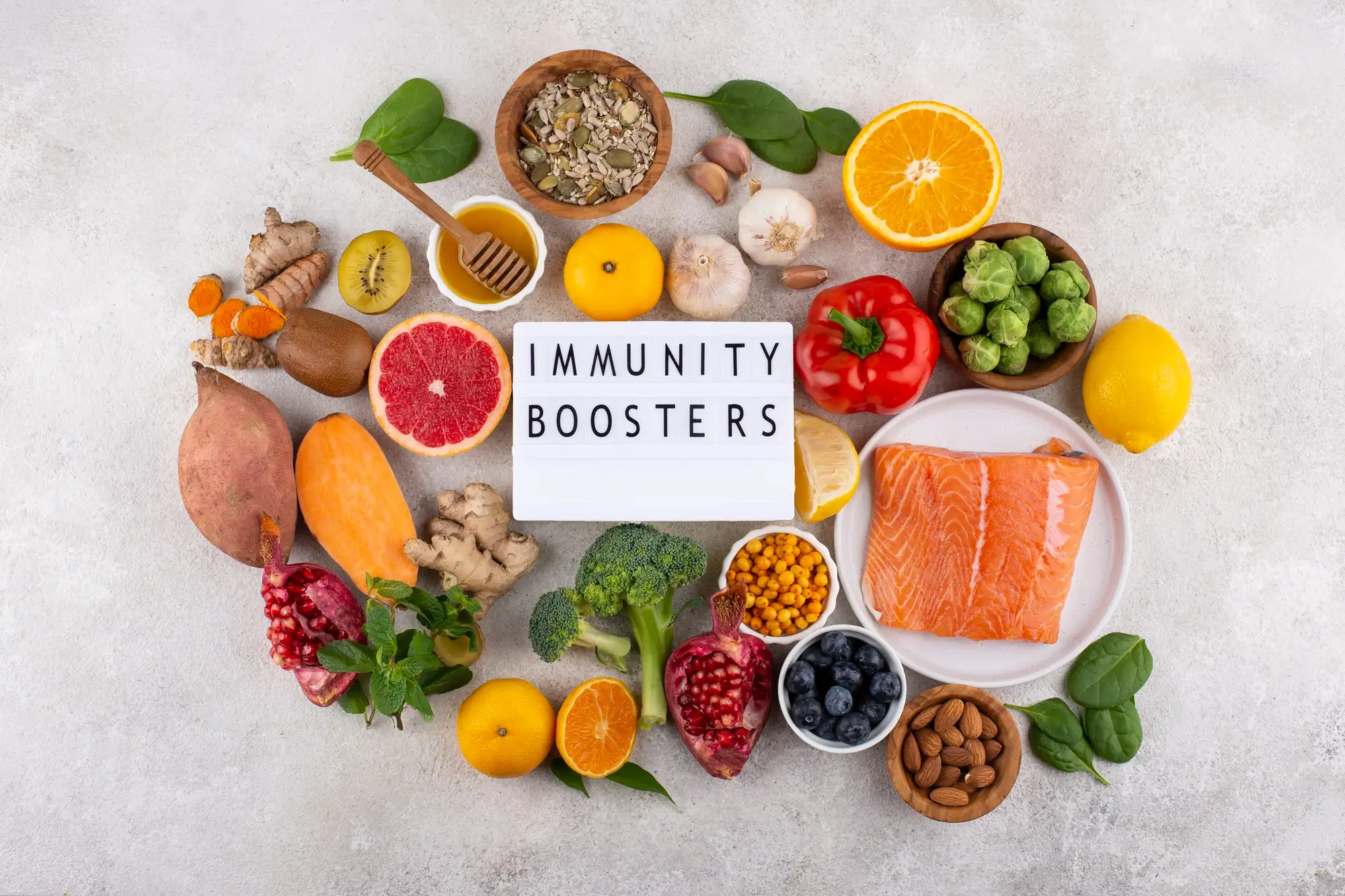 A variety of top immune-boosting foods including citrus, garlic, ginger, spinach, sweet potato, and broccoli arranged around a sign reading “Immunity Boosters”