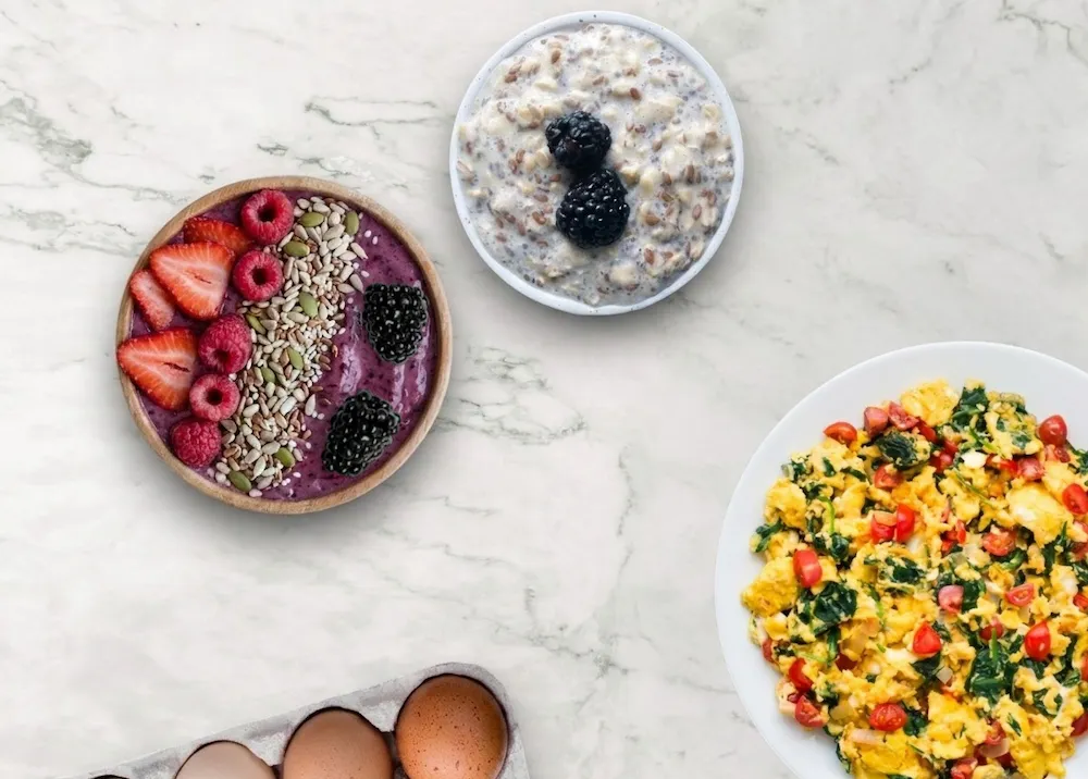 Overhead flat-lay collage of easy high-protein breakfast ideas featuring a mixed berry smoothie bowl with seeds, chia overnight oats, and vegetable scrambled eggs.