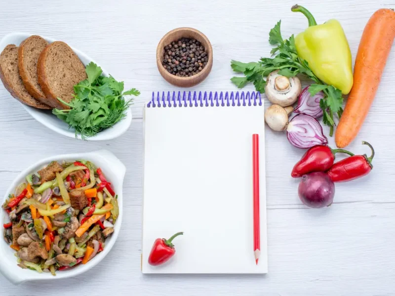 Colorful vegetables and open notebook showing My Pure Organics promise of clean, honest nutrition content